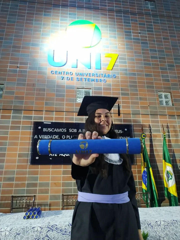 Ana Menires de beca e capelo segurando o canudo na formatura da UNI7